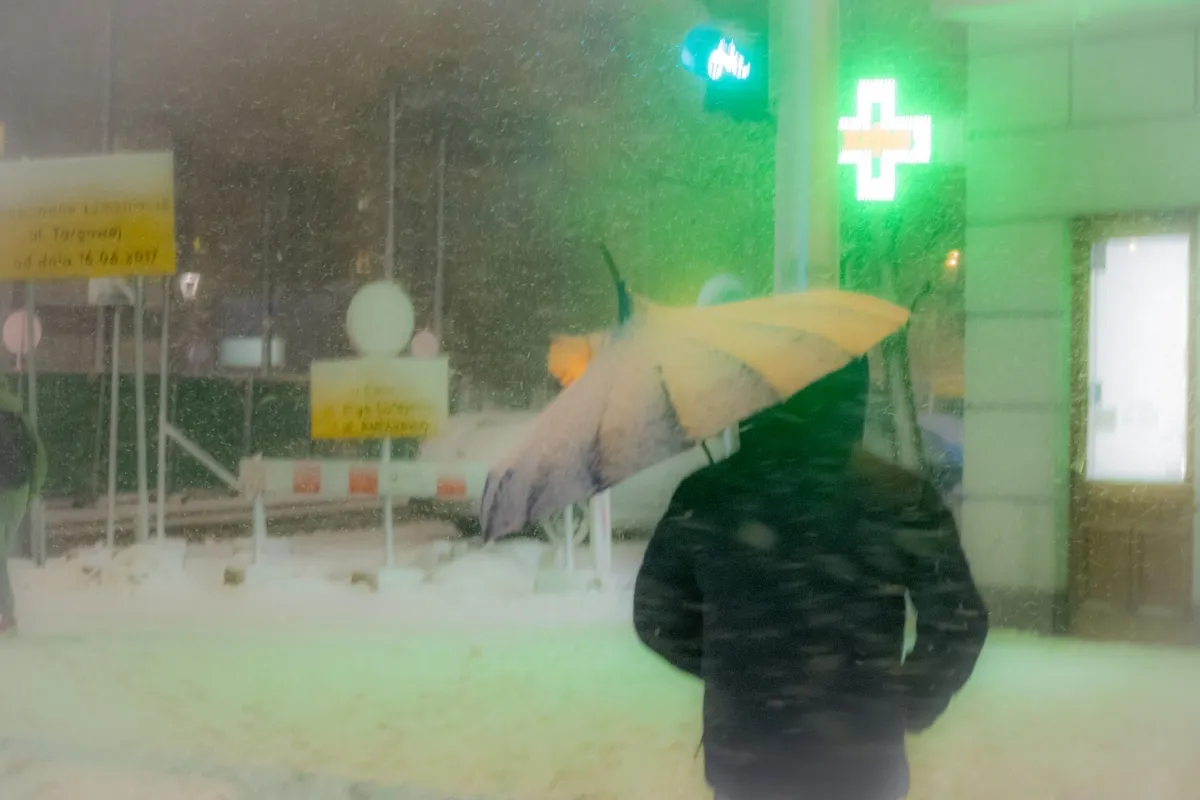 Person with a yellow umbrella in a misty street beneath green pharmacy lights